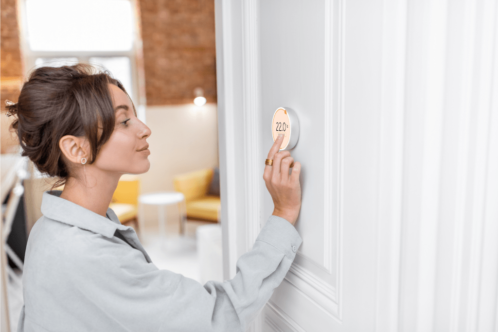 a woman adjusting the temperature on her smart thermostat

