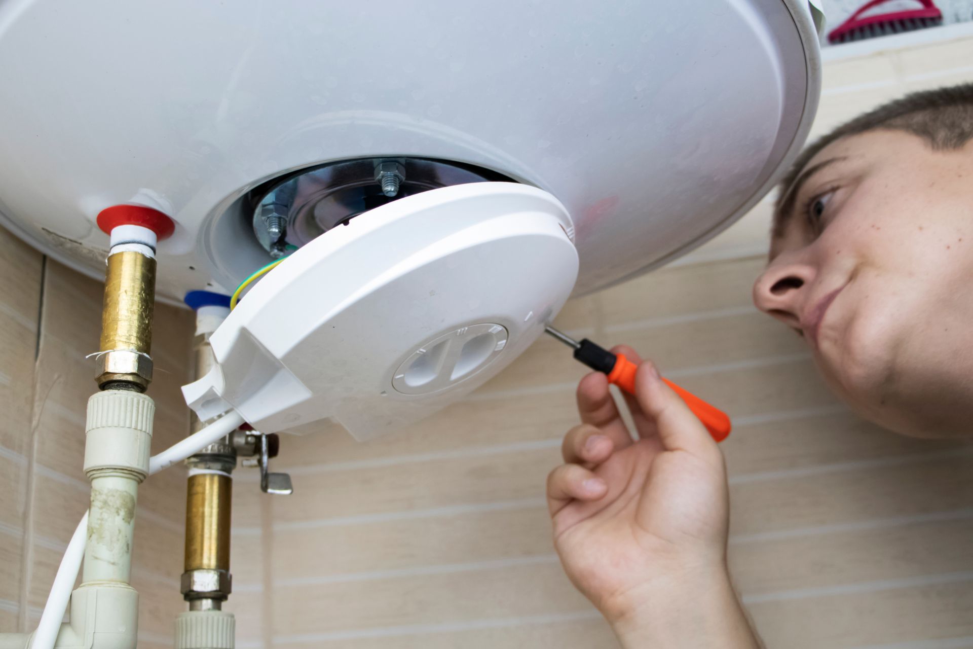 A man unscrews a water heater’s hatch with a screwdriver