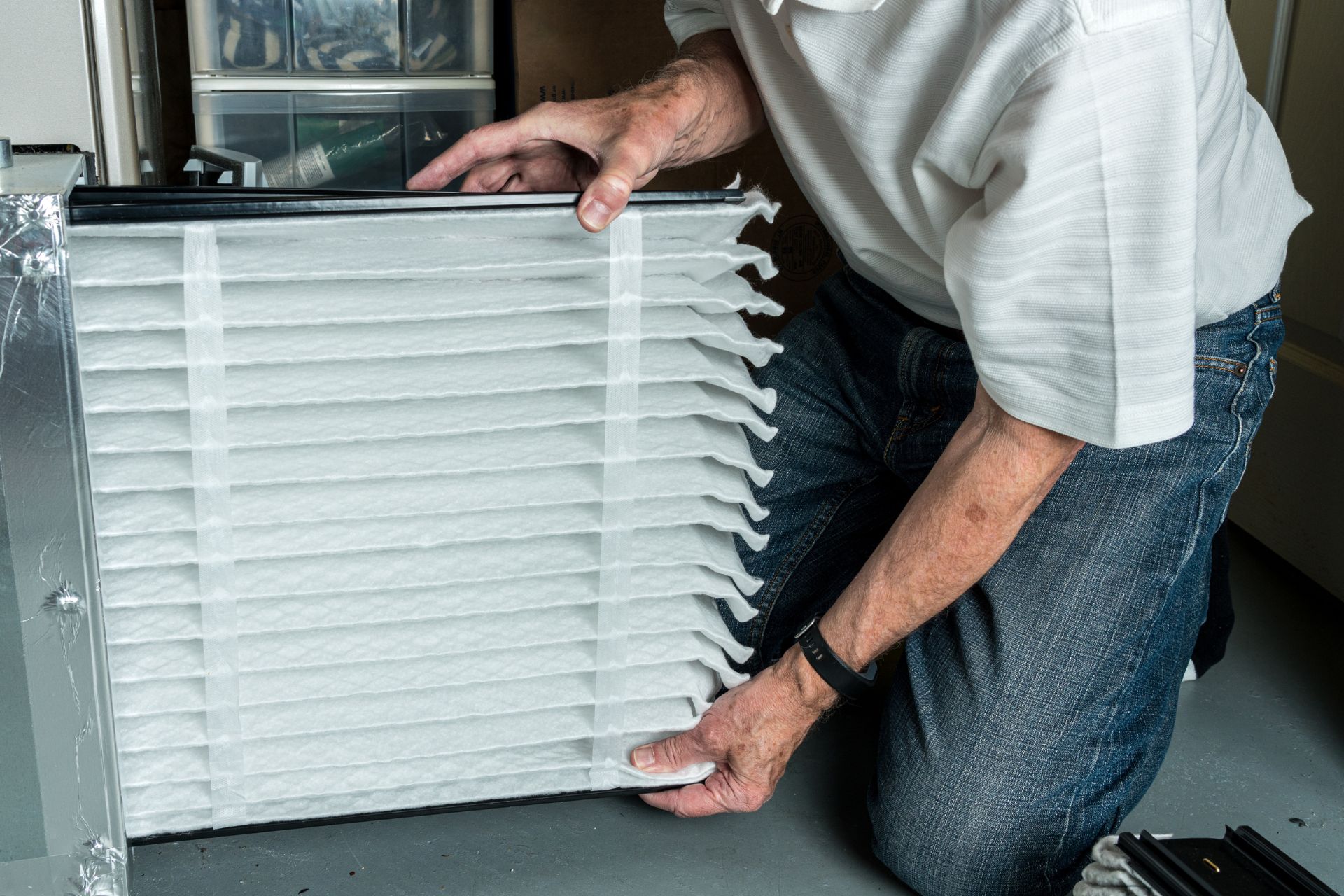 A homeowner inserts a clean filter inside their home’s furnace