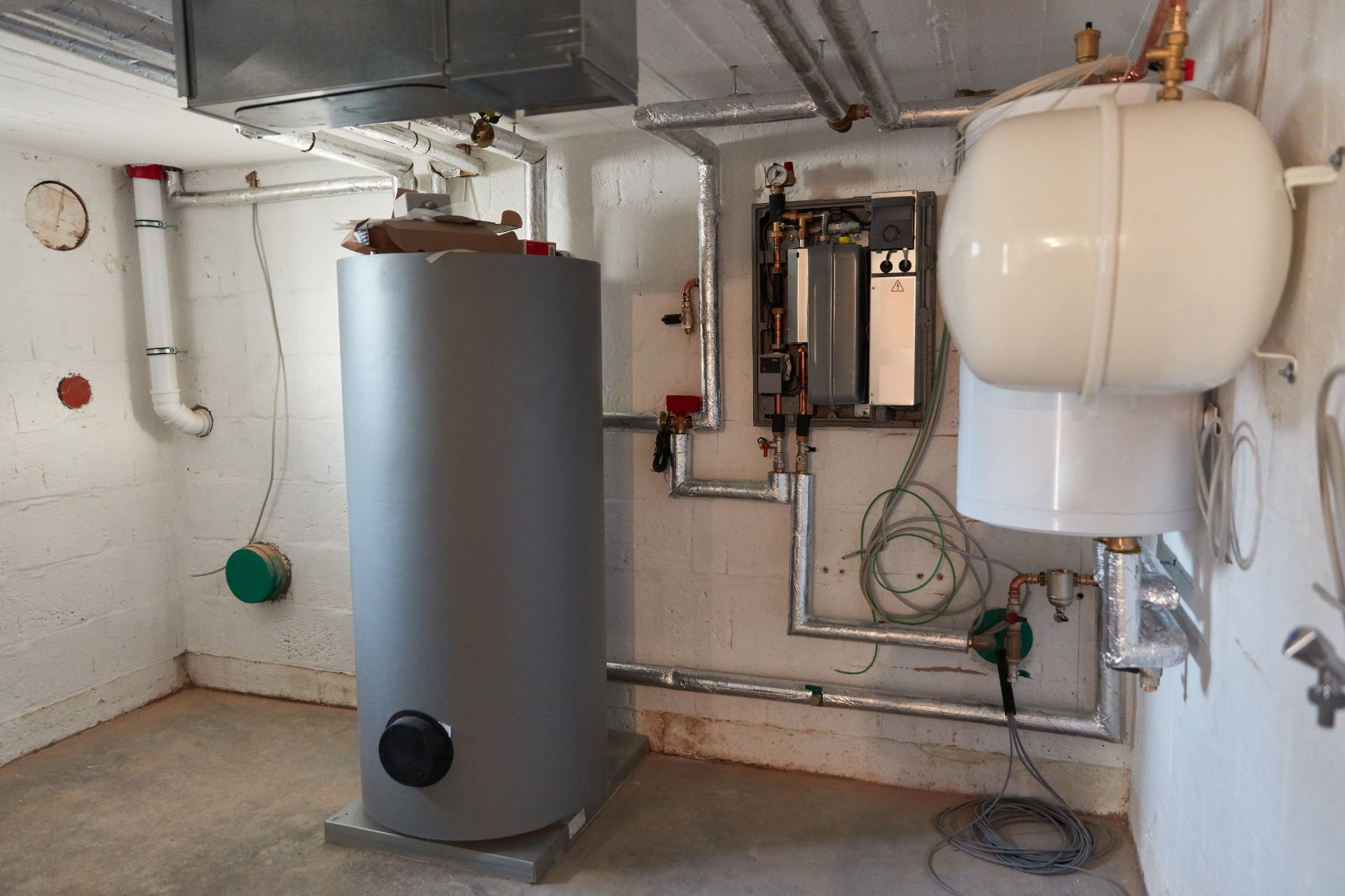 A silver boiler in a basement, and several supply lines and plumbing connect to it