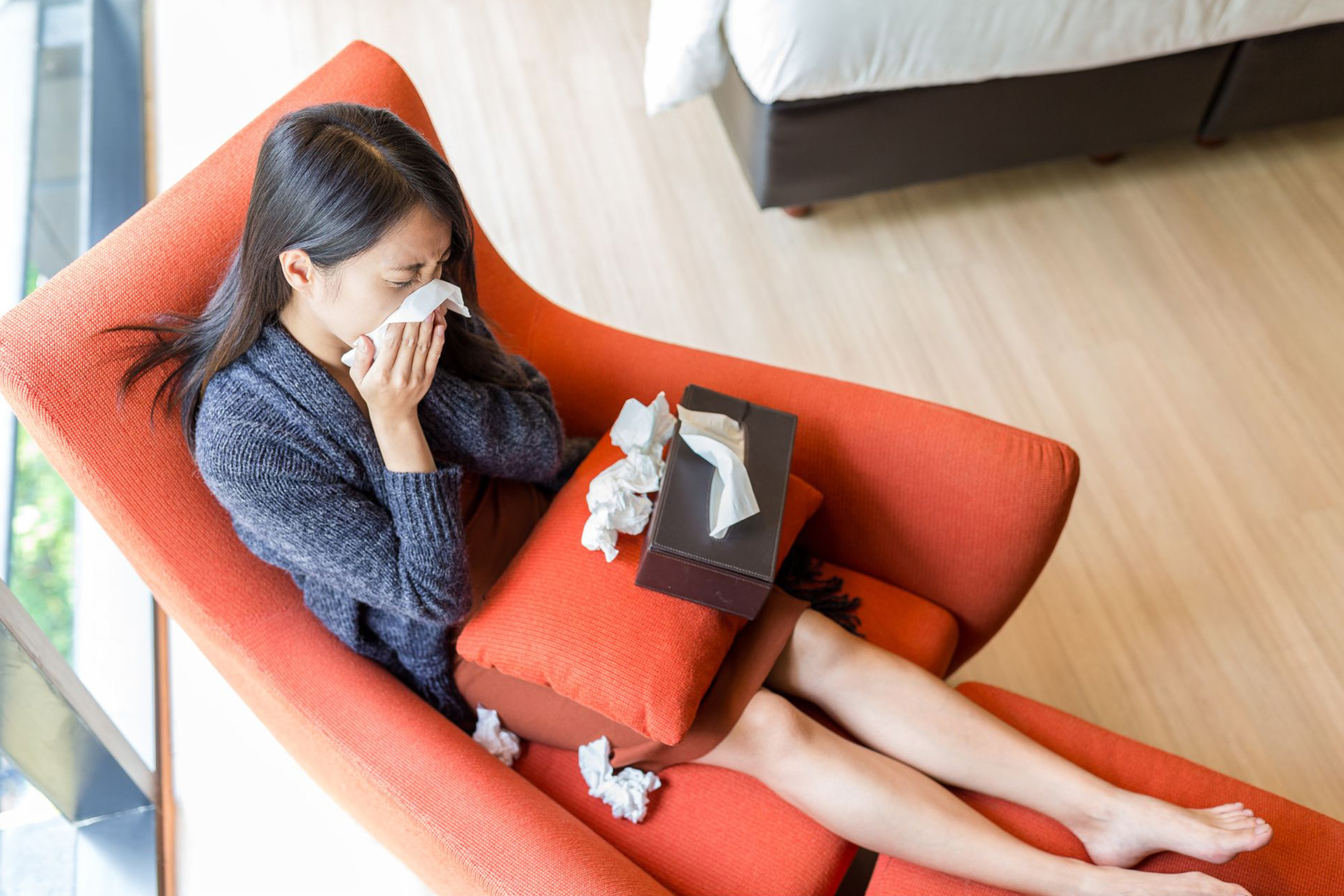 A woman sneezing into a piece of tissue paper sitting on an orange chair