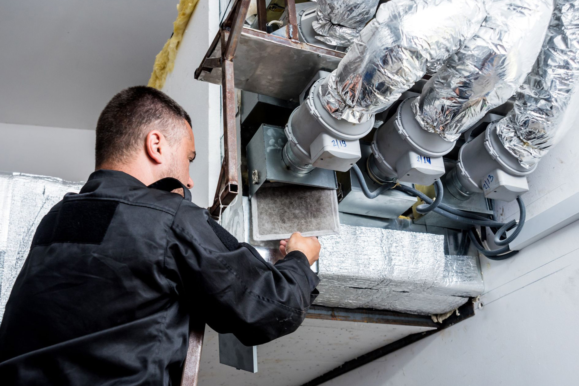 An HVAC technician removing an air filter from a ductwork and vent system