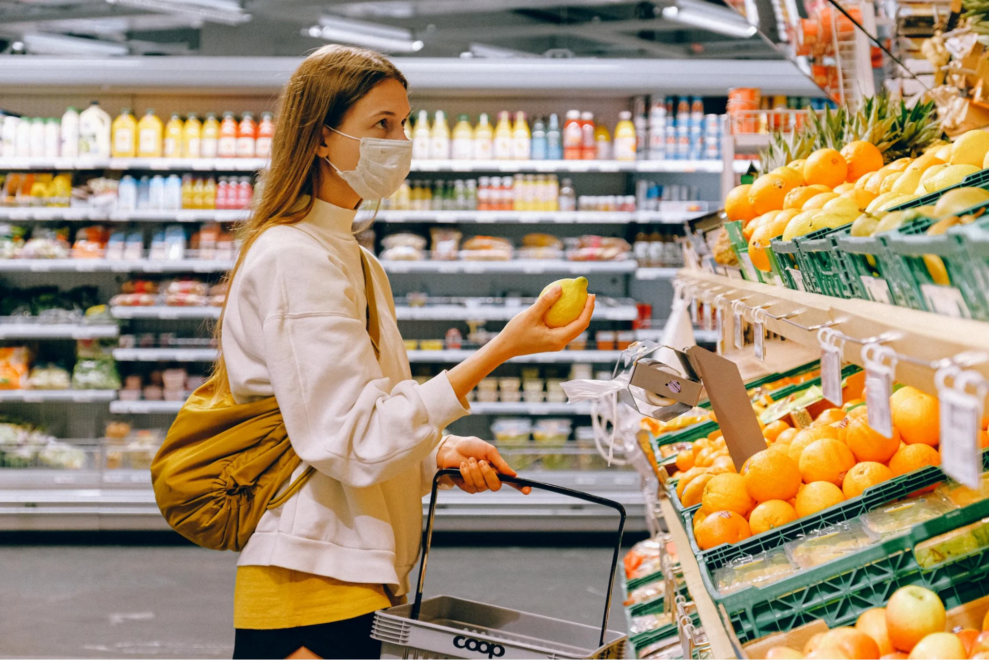 A woman standing in a grocery store holding a fruit in her hand, looking at price tags.