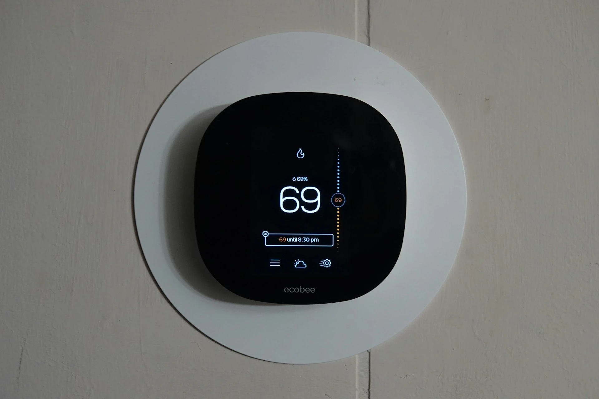 A modern black ecobee smart thermostat mounted on a white circular wall plate