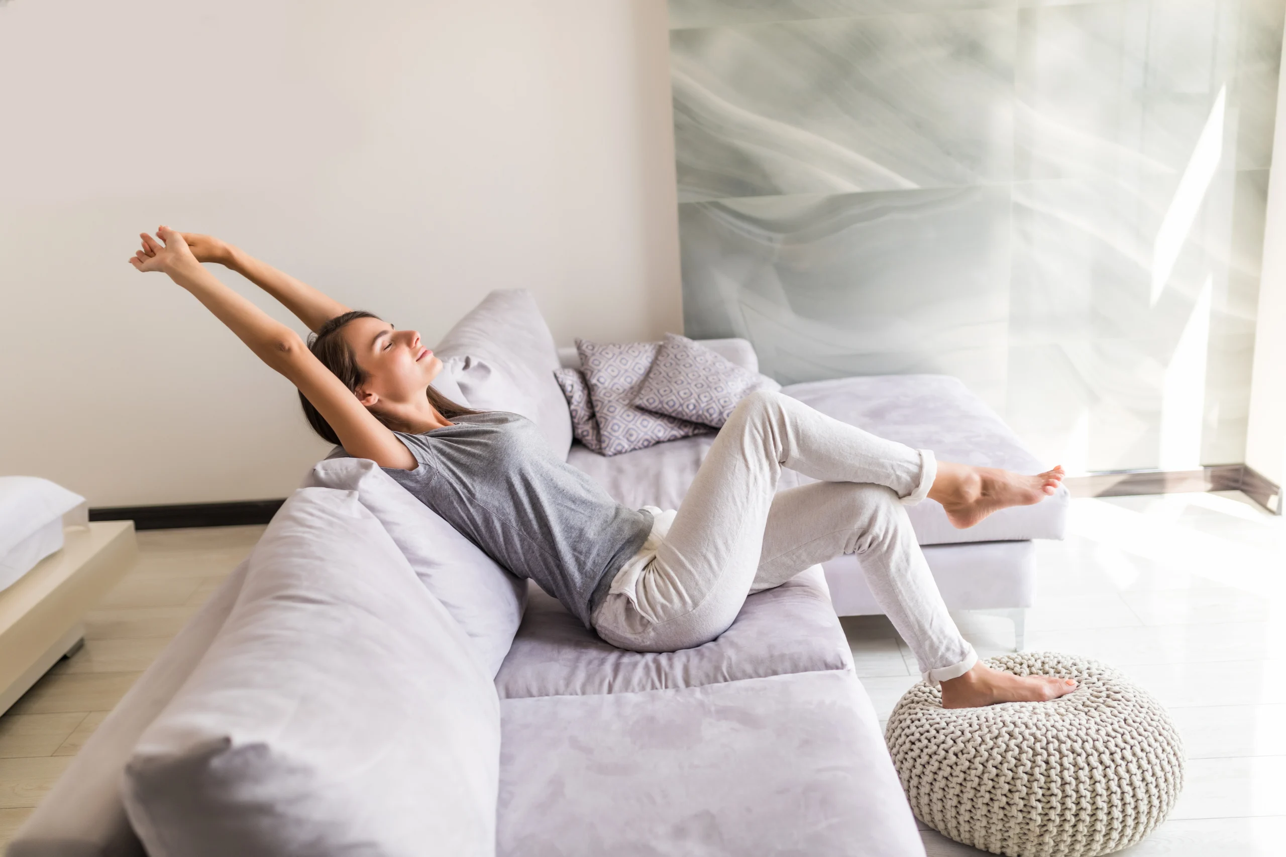 Woman stretching contentedly on a couch by a sunny window.