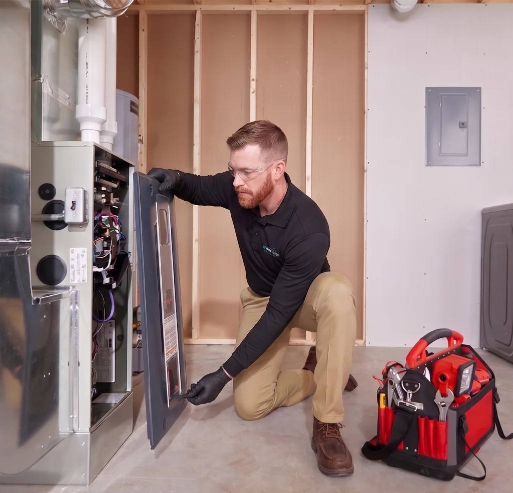 Kneeling worker servicing an open furnace panel beside a tool bag.